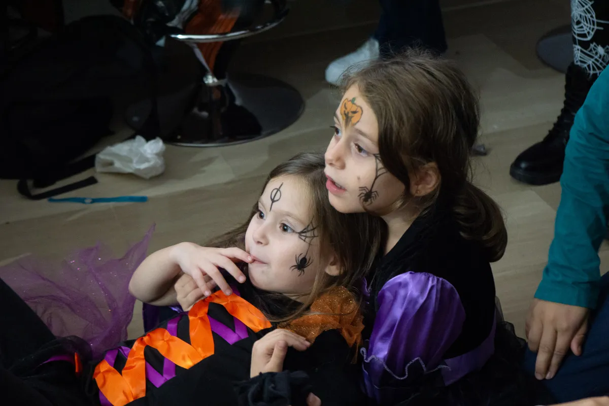 Bambine truccate a tema Halloween guardano lo spettacolo sedute a terra